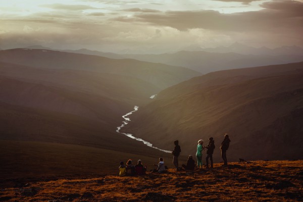 Big group of friends on mountain's top having rest and looging at sunset. Space for text