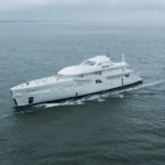 The hull of an Amels 60 superyacht under tow during construction at sea, showing the vessel’s exterior profile