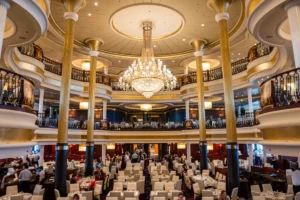 Luxurious multi-level dining hall on a Royal Caribbean cruise ship, featuring chandeliers, gold columns, and elegant seating for guests.