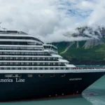 Holland America Line cruise ship sailing through Alaska fjords with mountains in the background