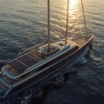 A sleek, modern 90-metre sailing superyacht with towering carbon-neutral DynaRig sails glides across calm tropical waters at sunrise. Expansive solar-panel surfaces shimmer across the deckhouse and hardtops, while the hull’s metallic deep-ocean blue finish reflects the golden sky. No exhaust is visible; only a faint wake and the soft curve of the sails disturb the mirror-like sea.