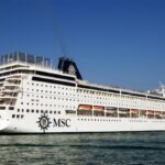 MSC Sinfonia cruise ship sailing in calm waters under clear blue skies, showing its white hull and multiple passenger decks
