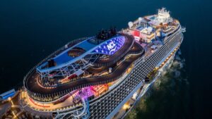 Aerial view of a Norwegian Cruise Line ship at night showing the illuminated NCL logo and the onboard go-kart racetrack on the top deck