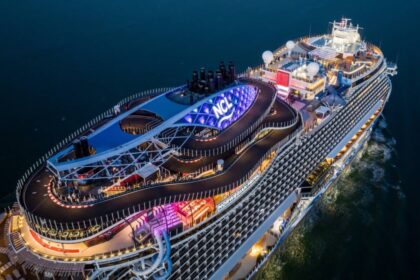 Aerial view of a Norwegian Cruise Line ship at night showing the illuminated NCL logo and the onboard go-kart racetrack on the top deck