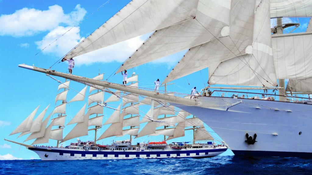 Crew members climb the rigging of a Star Clippers sailing ship as its full sails are raised at sea