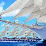 Crew members climb the rigging of a Star Clippers sailing ship as its full sails are raised at sea