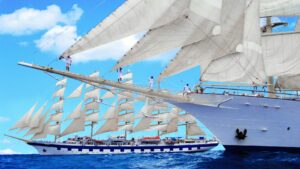 Crew members climb the rigging of a Star Clippers sailing ship as its full sails are raised at sea