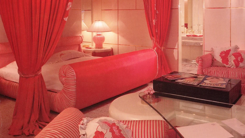 The Ruby Suite bedroom aboard Trump Princess featuring red upholstery, patterned fabrics, and a private seating area