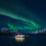 Cruise ship illuminated at night beneath the Northern Lights over the Lofoten Islands, Norway