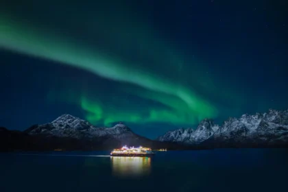 Cruise ship illuminated at night beneath the Northern Lights over the Lofoten Islands, Norway