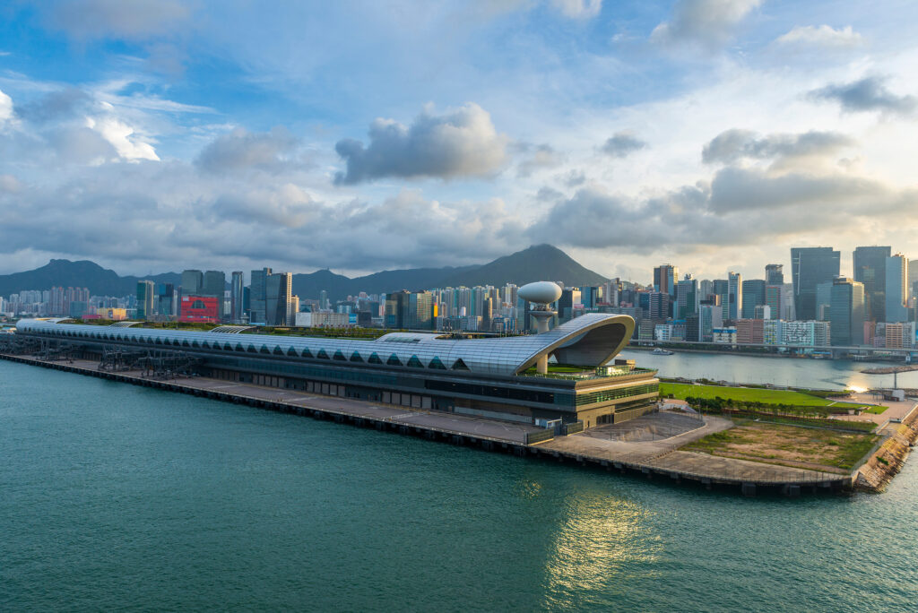 Aerial view of Hong Kong’s Kai Tak Cruise Terminal with the city skyline and Victoria Harbour in the background, highlighting the waterfront cruise facility and surrounding urban landscape.