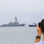 A US Navy warship operates near Venezuelan waters as regional tensions lead to flight cancellations and travel disruptions affecting Caribbean cruise passengers.