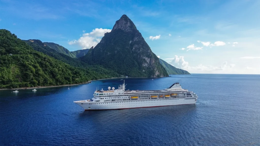 Villa Vie Odyssey residential cruise ship sailing near Saint Lucia with the Pitons rising in the background under clear blue skies.